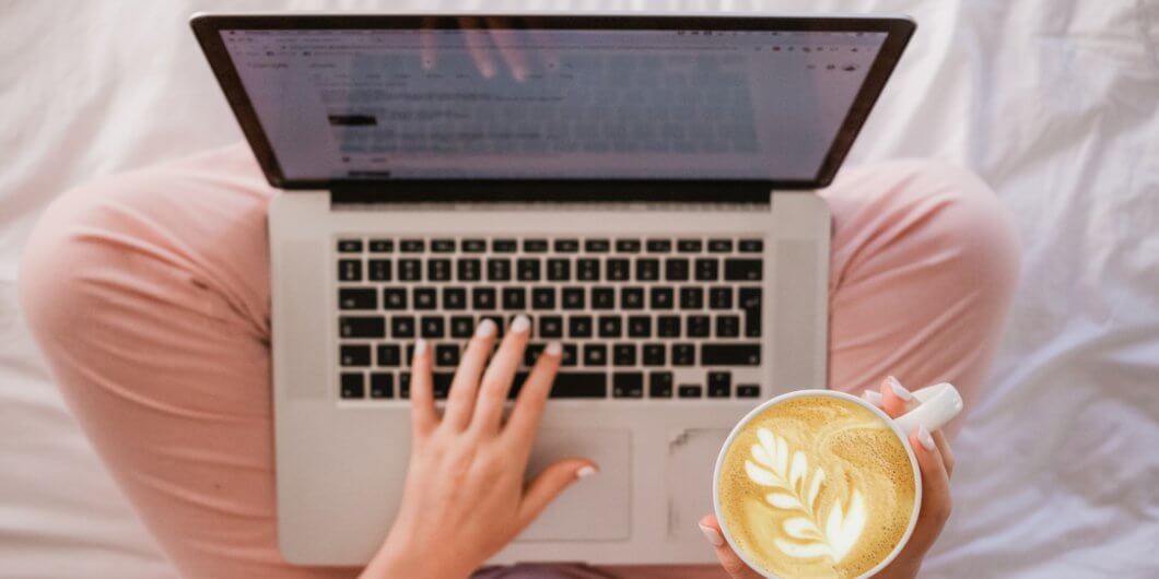 woman in pink pans with a laptop and latte