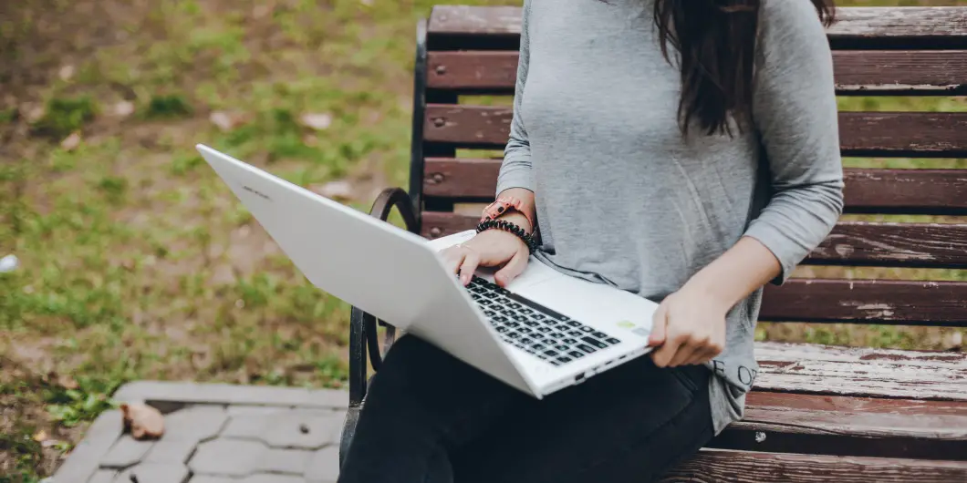 girl in gray sweater sitting on bench laptop