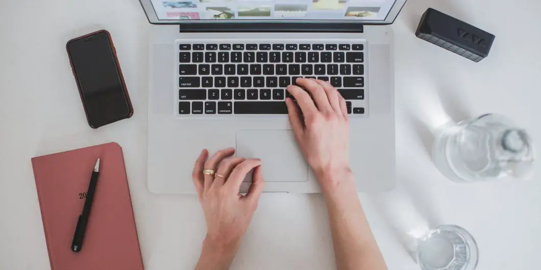 This is picture of a computer with a woman's hands typing on it. There is a white backdrop and this post is about How To Join Tailwind Tribes