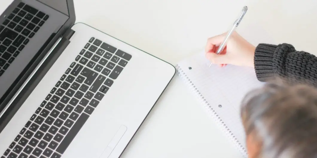 white laptop on white desk with woman writing in front of it Christian blog niche ideas